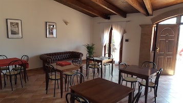 A dining area with a brown leather sofa, wooden tables, and chairs. There are two framed pictures on the wall and a potted plant.