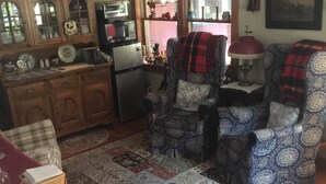 Un salon chaleureux avec une cheminée, un coin repas avec une table et des chaises, et une cuisine dotée de meubles en bois et d’un réfrigérateur.