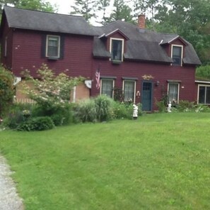 A two-story red house with a dark roof, a front porch, and a well-maintained lawn.