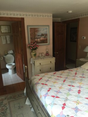 A bedroom with a bed, a dresser, a painting, a toilet, and a door leading to another room.