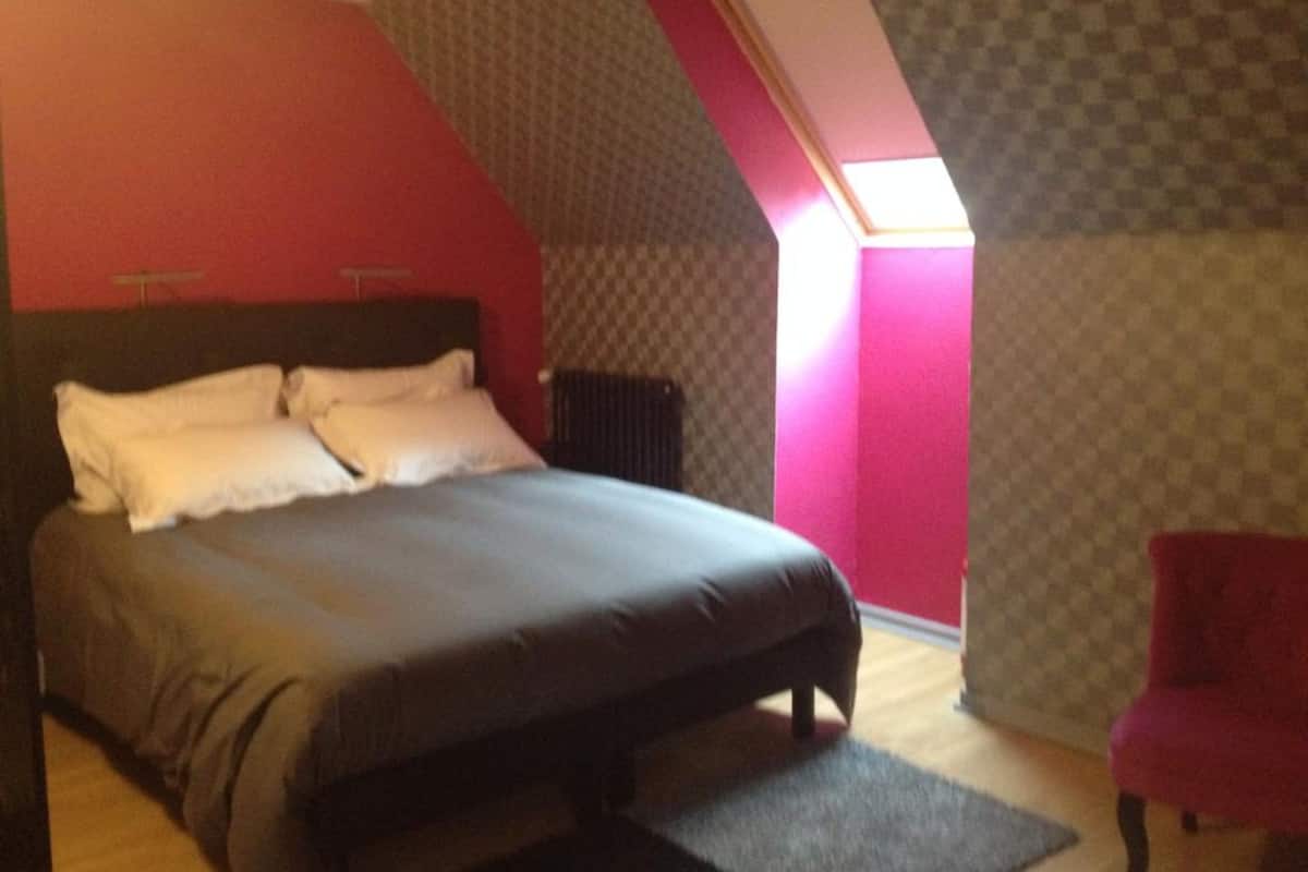 Un dormitorio con una cama, una silla roja y un techo inclinado con ventana.