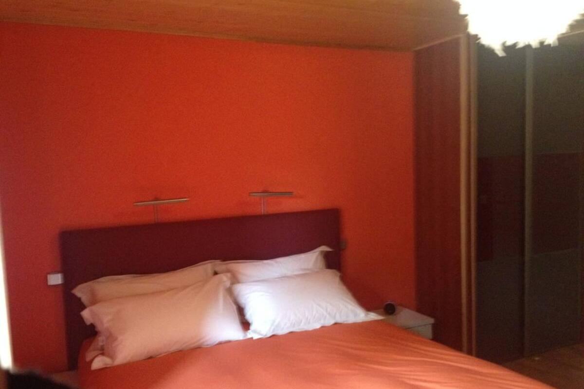 Un dormitorio con pared roja, cabecera de madera y cama con ropa de cama blanca.