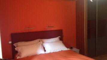 Un dormitorio con pared roja, cabecera de madera y cama con ropa de cama blanca.