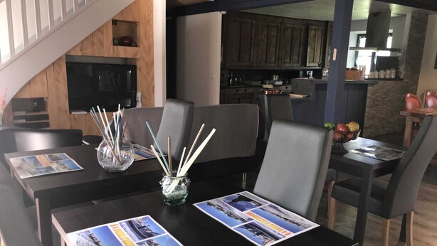 Ruokailutila, jossa on neljälle katettu pöytä, ja siellä on tarjolla lehtiä sekä lasinen maljakko, jossa on oksia.