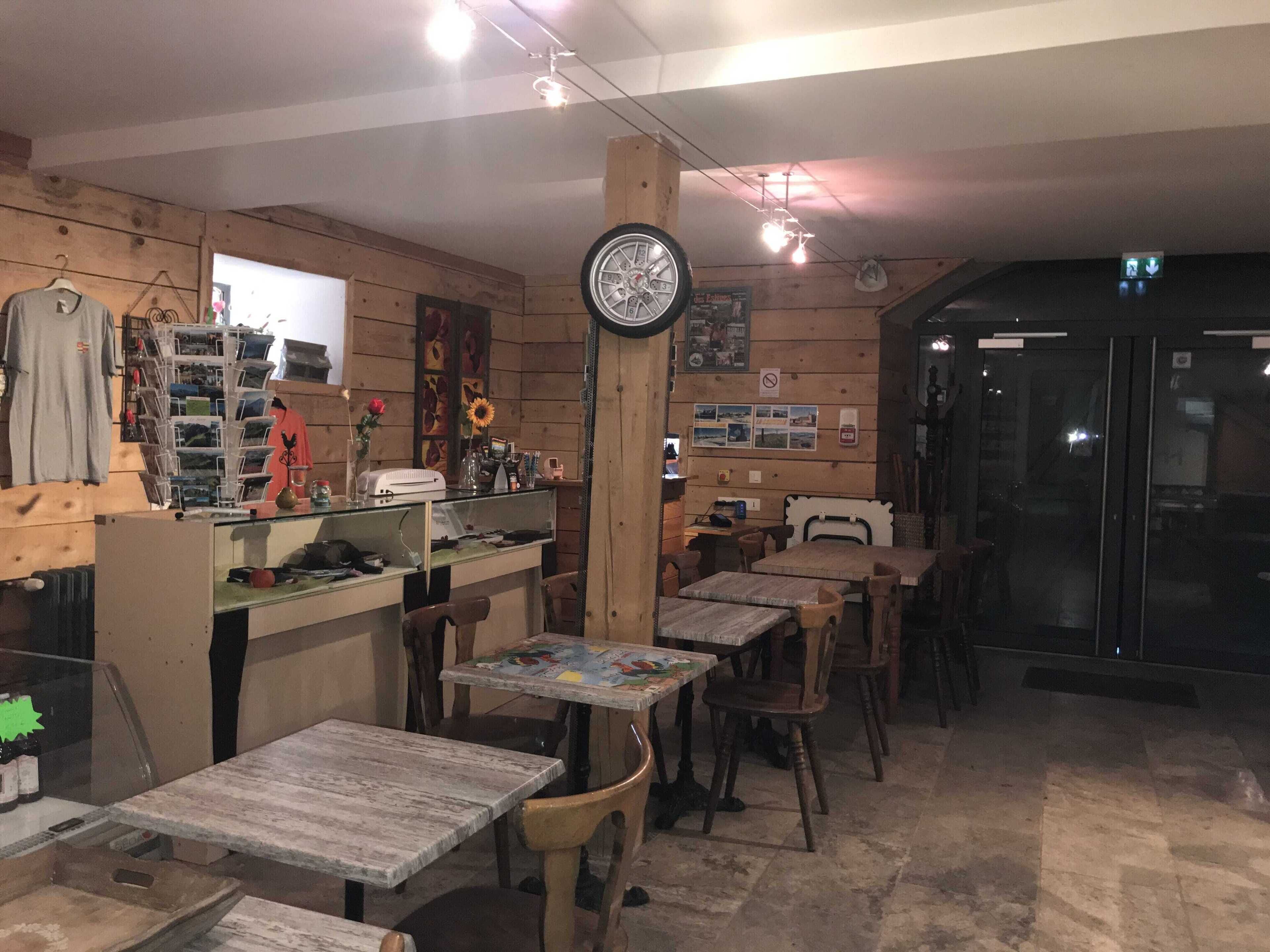 A cozy restaurant interior with wooden walls, multiple tables and chairs, a counter with various items, and a clock on the wall.