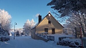 Lumipeitteinen talo, jossa on kalteva katto, savupiippu ja pieni kuisti.