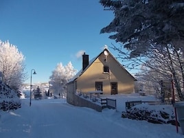A snow-covered house with a sloped roof, a chimney, and a small porch.