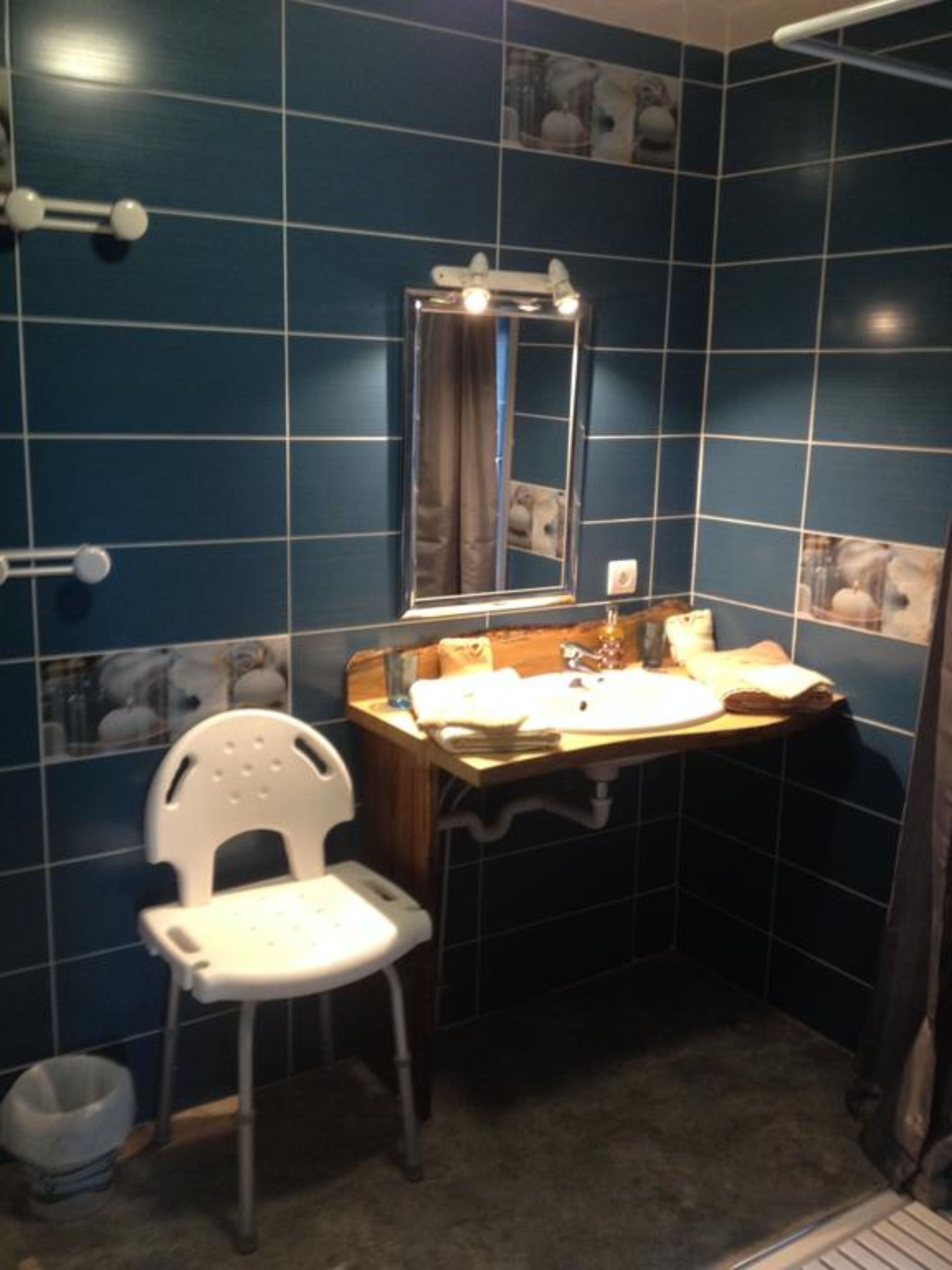 Een badkamer met blauwe tegels, een witte stoel, een wastafel met spiegel en een handdoekrek.