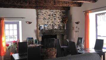 A rustic room with a stone fireplace, wooden beams, a dining table with chairs, and a window with curtains.