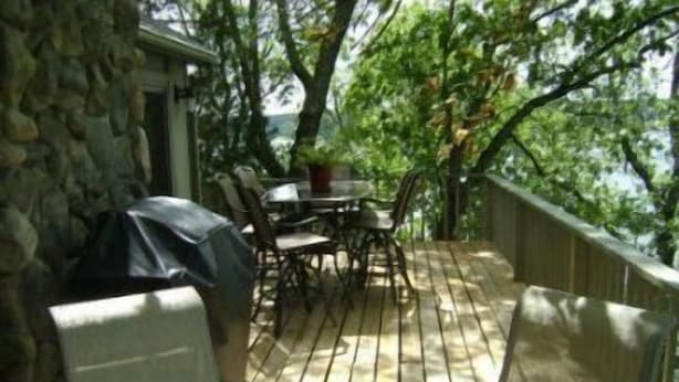 Un patio techado al aire libre con mesa y sillas, rodeado de muros de piedra y árboles.
