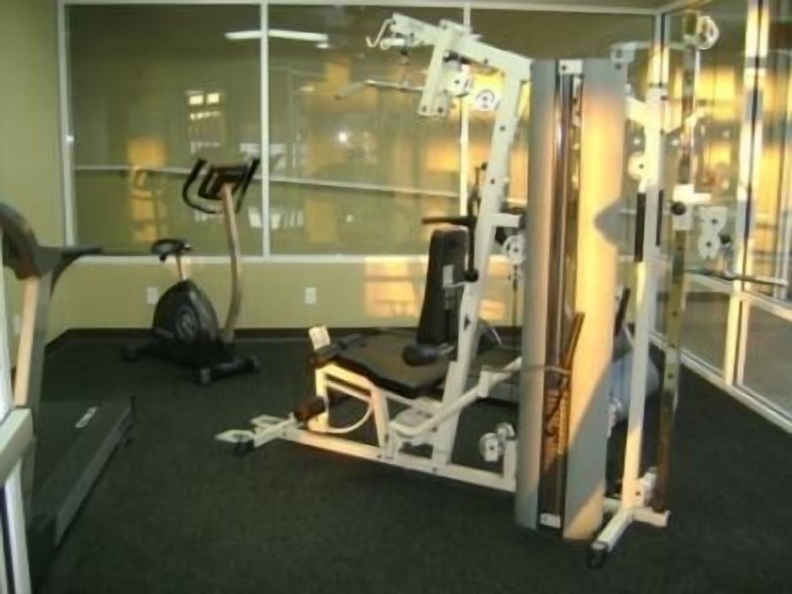 Un gimnasio con equipo de ejercicio, cinta de correr y pared espejada.