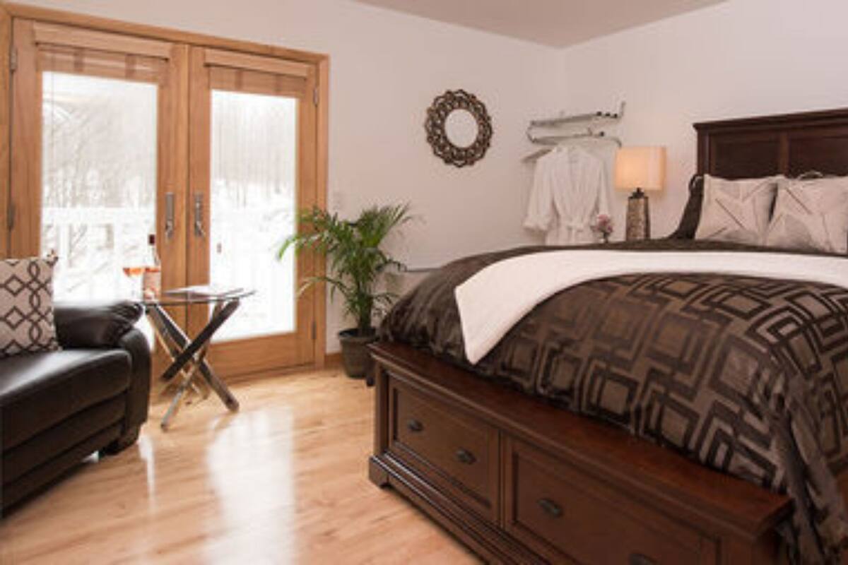 A bedroom with a large bed, wooden headboard, and a dresser. There is a small table with a plant and a lamp.