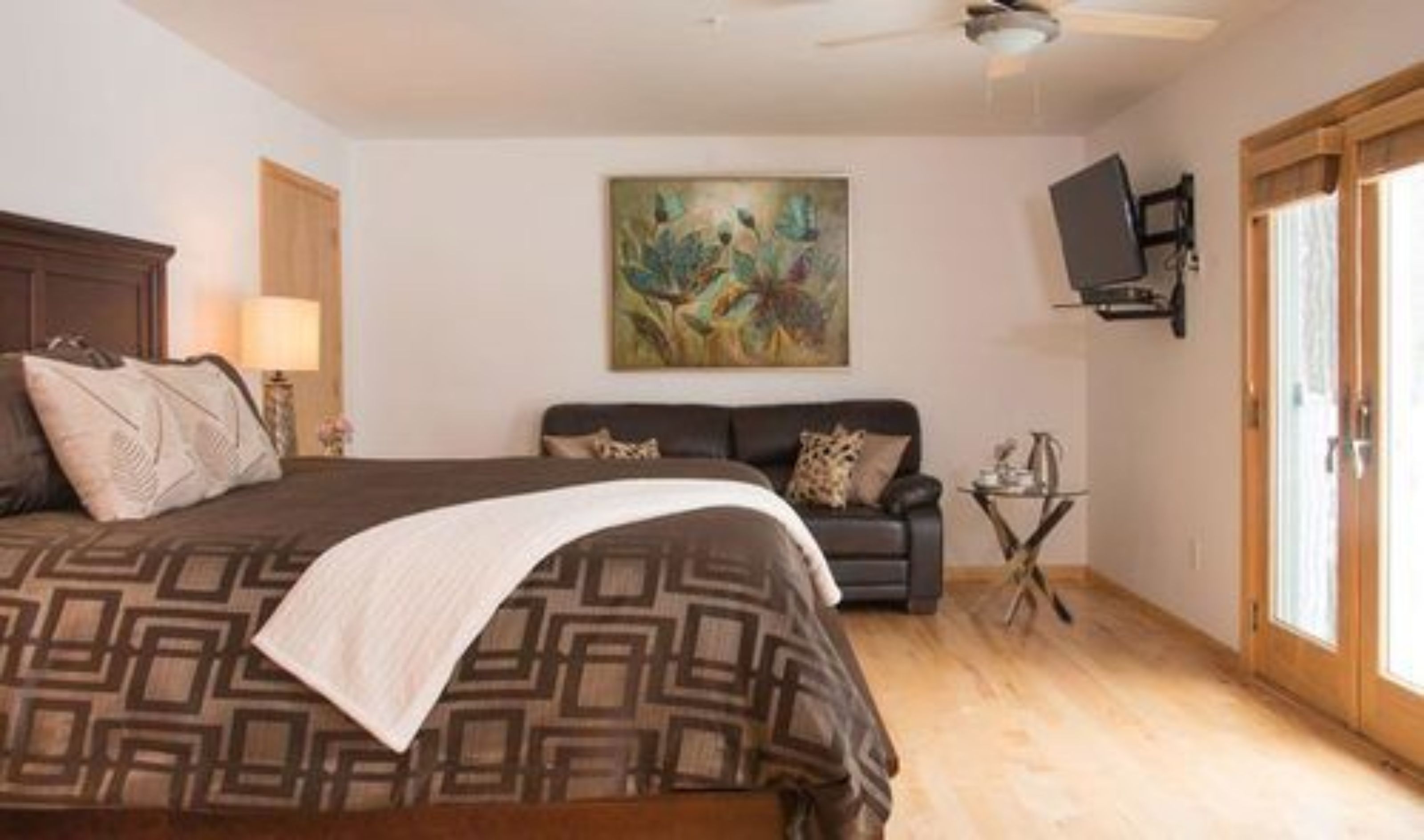 A bedroom with a large bed, a sofa, a painting on the wall, and a television mounted on the wall.