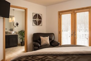 Une chambre à coucher comprenant un lit, une chaise, une œuvre d’art accrochée au mur et une fenêtre avec des stores.