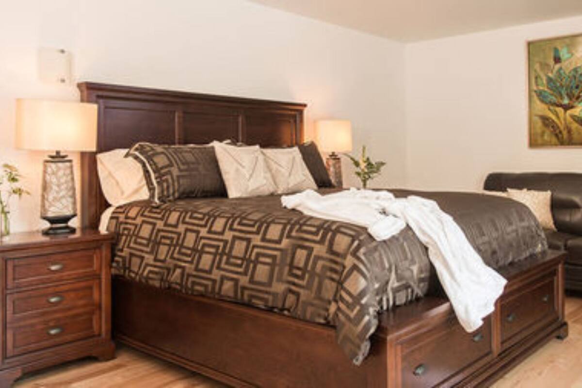 A bedroom with a large bed, two bedside tables, a chair, and a painting on the wall.