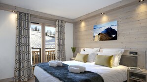 Een moderne slaapkamer met een groot bed, houten wanden, uitzicht op een besneeuwd landschap en een schilderij van bergen.
