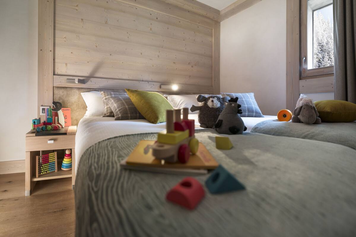 A bedroom with a wooden headboard, a bed with a patterned bedspread, and a window with a view of trees.