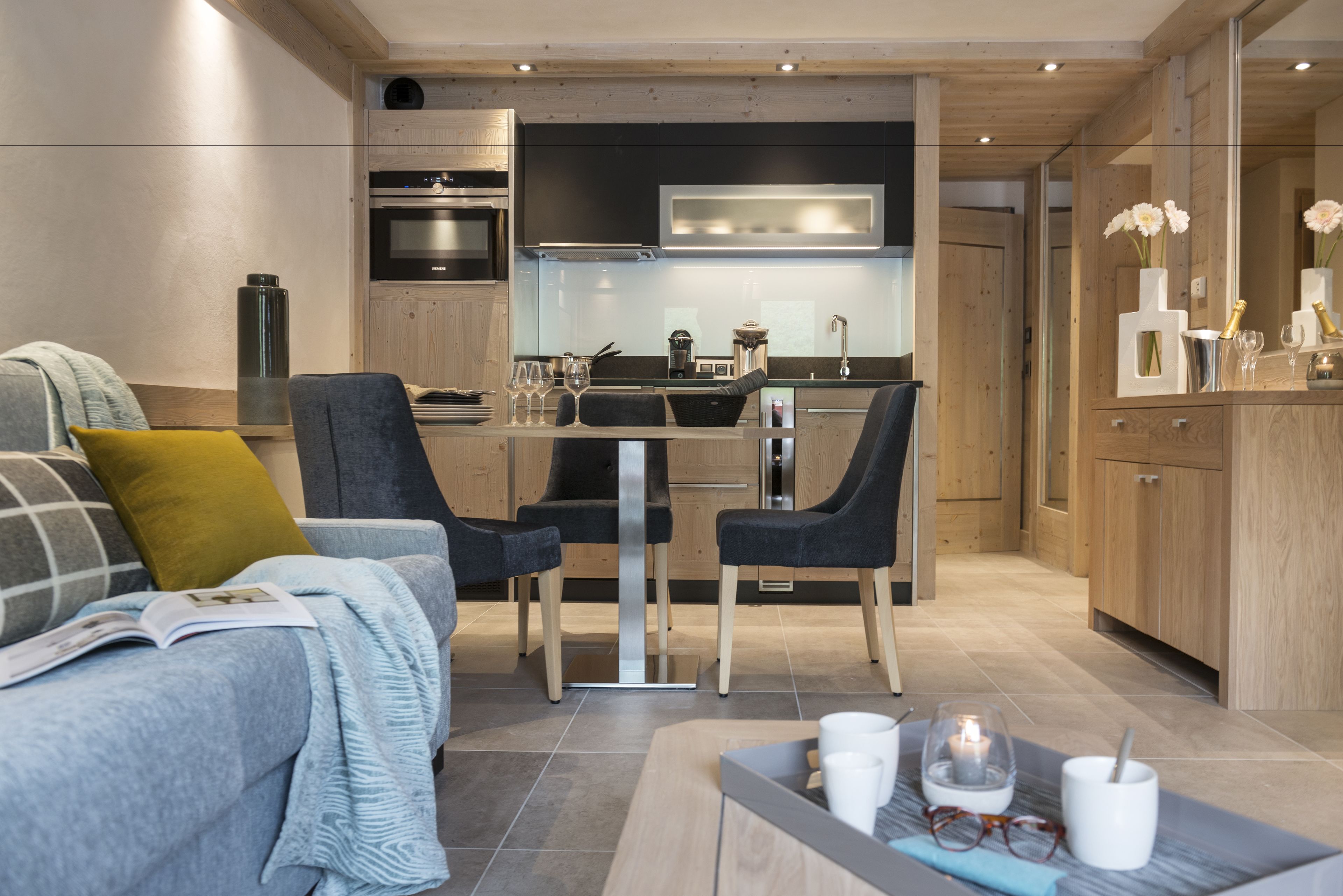 Une cuisine moderne dotée d’appareils électroménagers intégrés, un coin repas avec deux chaises et un espace salon confortable avec un canapé et une table basse.