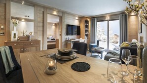 Een modern interieur met een houten eettafel, een aan de muur bevestigde televisie en uitzicht op met sneeuw bedekte bomen door grote ramen.