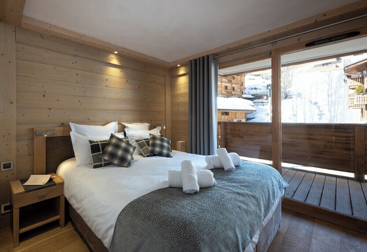 A wooden-paneled room with a bed, a nightstand, and a large window.