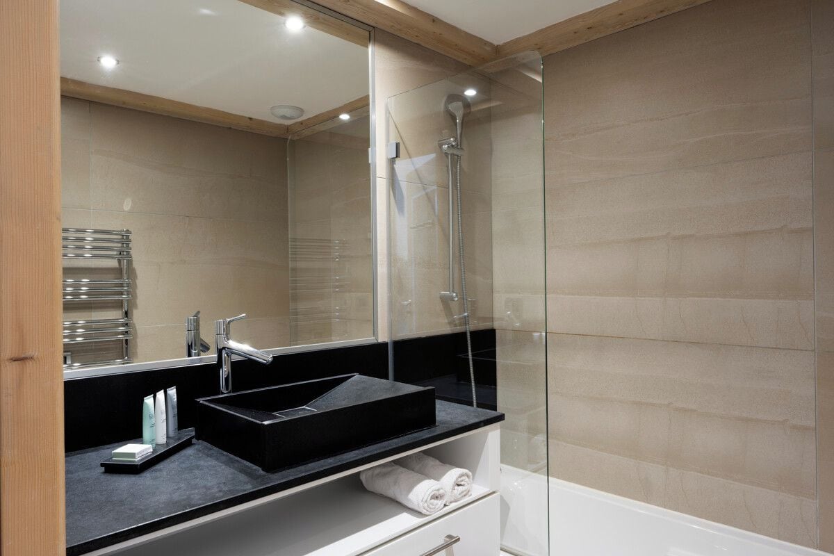 A modern bathroom with a black sink, a glass shower enclosure, and a white bathtub.