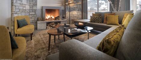 A cozy living room with a stone wall, a fireplace, a sofa, and a view of a snowy landscape.