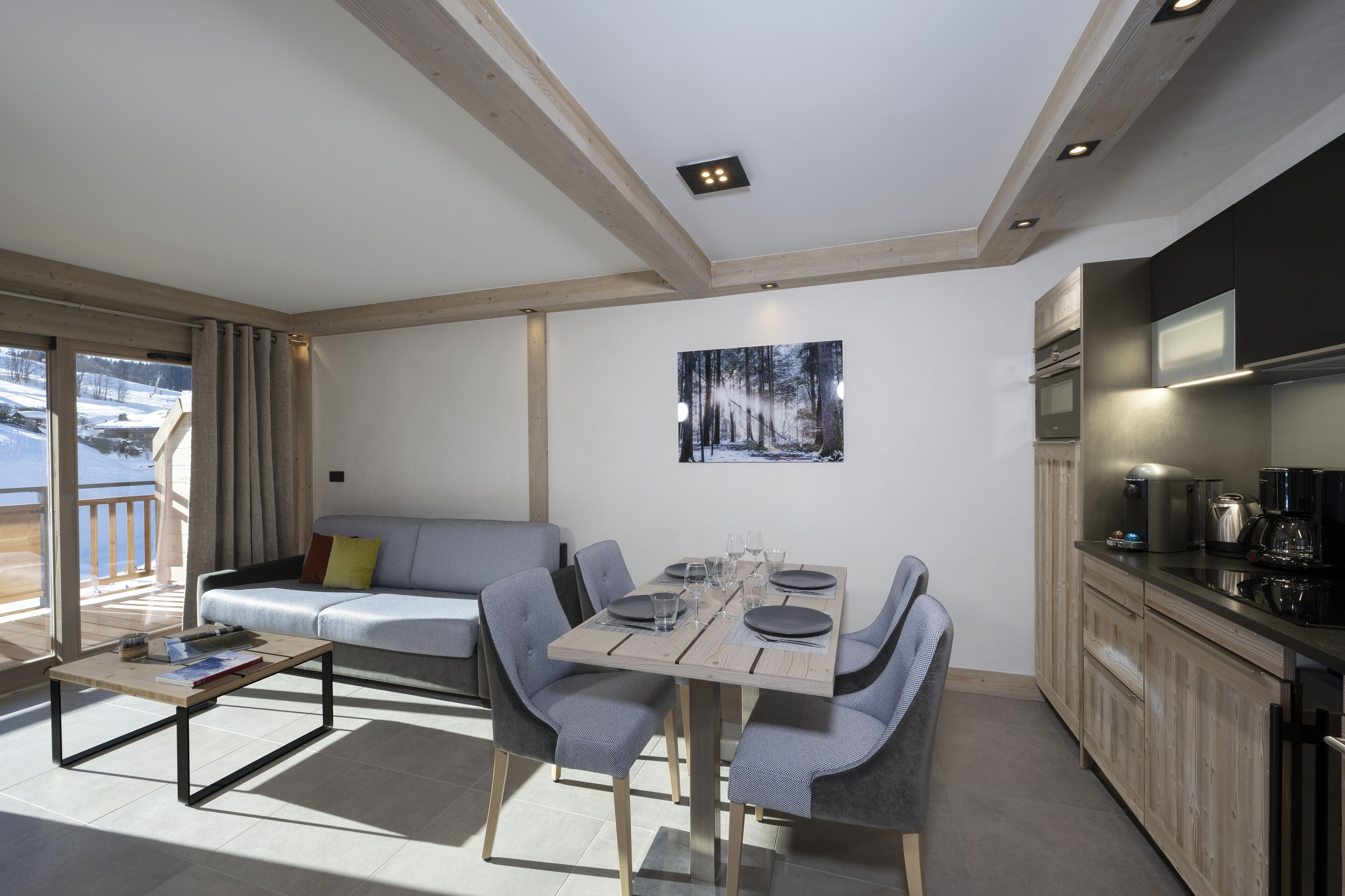 Una sala de estar moderna con una mesa de comedor preparada para cuatro personas, un sofá y una cocina equipada.