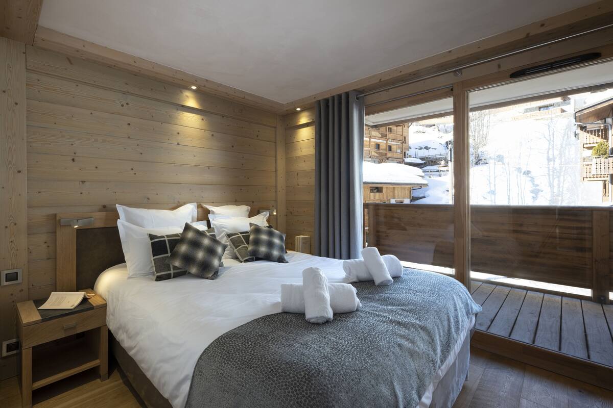 A wooden-paneled bedroom with a large bed, a nightstand, and a window with a view of a snowy village.
