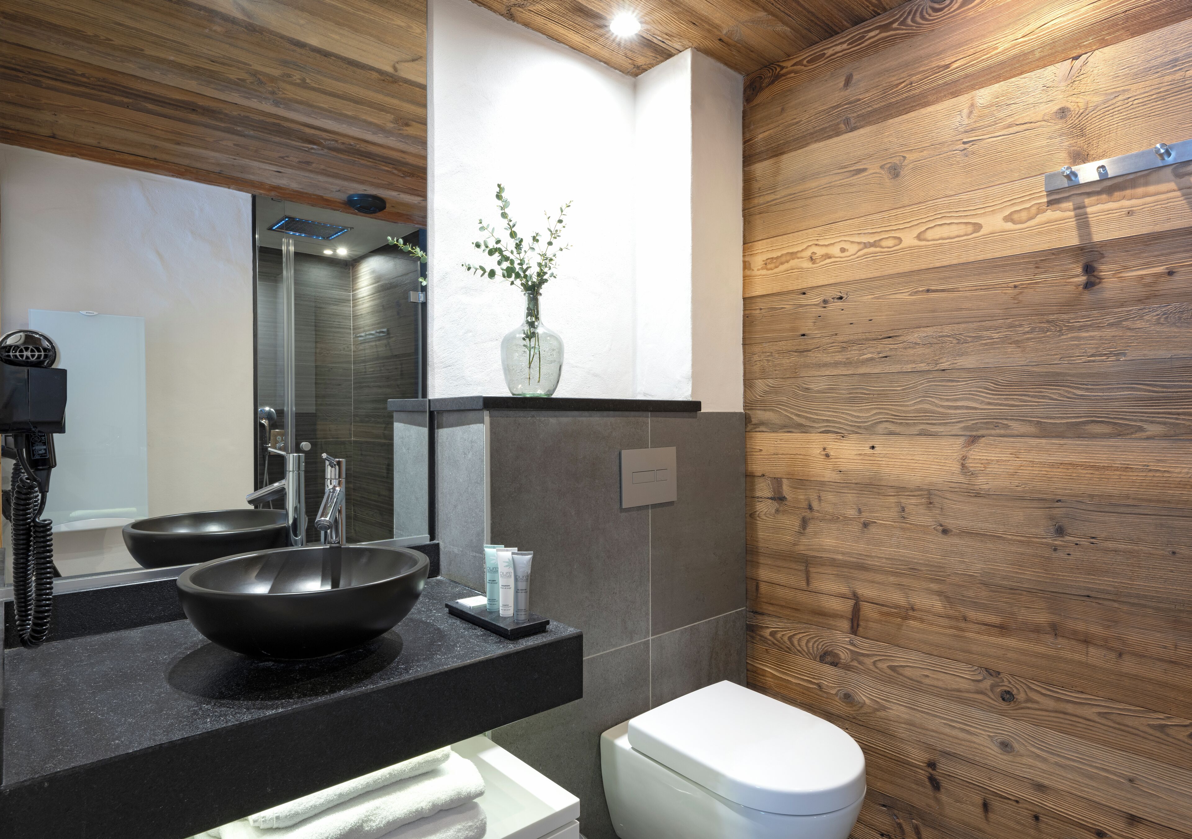 A modern bathroom with a black sink, a white toilet, and a wooden wall.