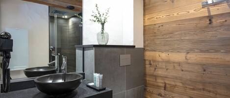 A modern bathroom with a black sink, a white toilet, and a wooden wall.