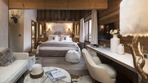 Een gezellige slaapkamer met een groot bed, een bureau en een stoel. Er is een open haard, een televisie en een raam met gordijnen.