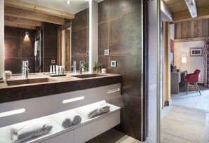 A modern bathroom with a large mirror, dual sinks, and a built-in bench with towels. - MGM Hôtels & Résidences – Résidence Le Cristal de Jade (Chamonix-Mont-Blanc)