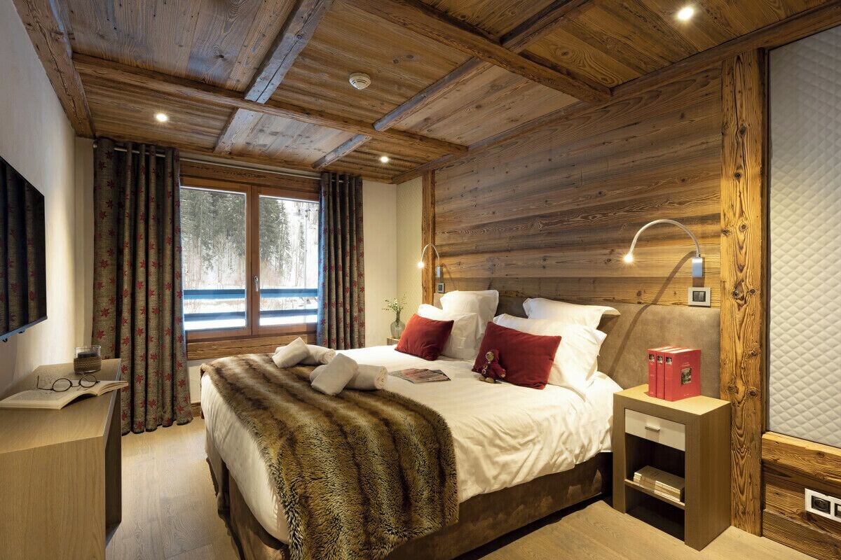 A wooden-paneled bedroom with a bed, bedside table, and a window with curtains.
