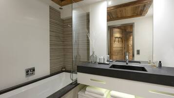 A modern bathroom with a glass shower enclosure, a wooden ceiling, and a large mirror reflecting a wooden door.