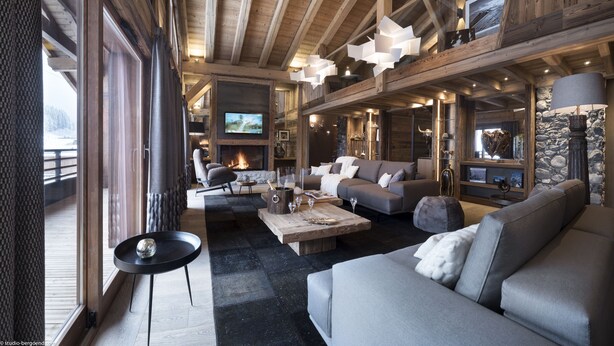Een gezellige woonkamer met een open haard, comfortabele zitplaatsen en een groot raam met uitzicht op een besneeerd landschap.
