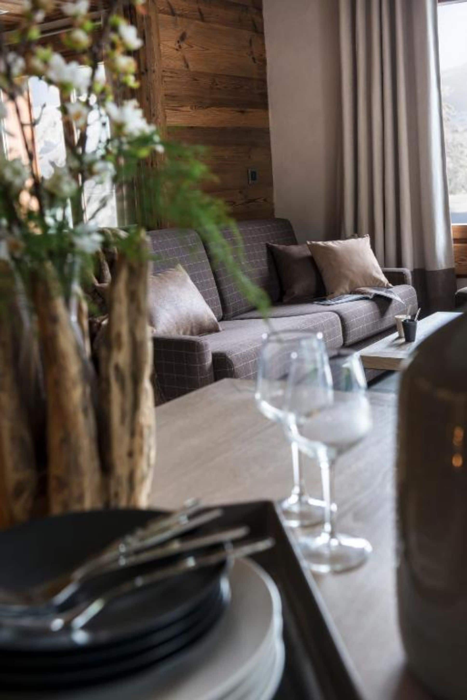 A cozy living area with a sofa, a dining table set with plates and a wine glass, and a view of the outdoors.