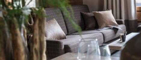 A cozy living area with a sofa, a dining table set with plates and a wine glass, and a view of the outdoors.