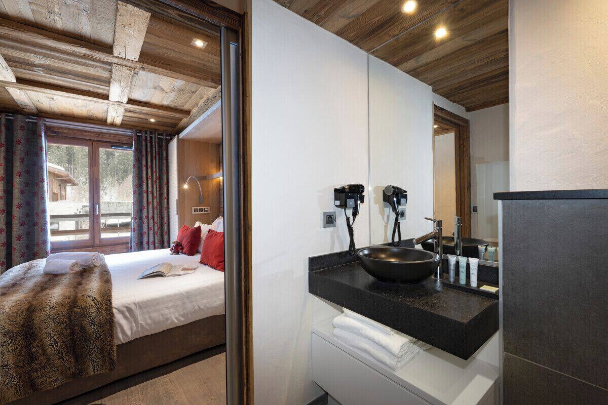 A modern hotel room with a large bed, a wooden ceiling, a black sink, and a window with curtains.