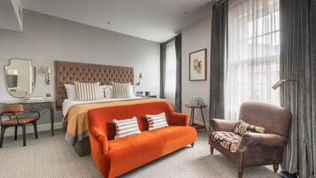 A hotel room with a large bed, a sofa, a chair, a desk, and a small table.