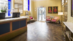 A reception area with a marble counter, a herringbone-patterned floor, and a large arched window with blue-tinted glass. - Harbour Hotel Bristol (Bristol)