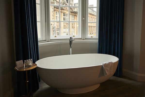A modern bathroom with a freestanding bathtub, a window with a view of buildings, and a small table with toiletries. - Harbour Hotel Bristol (Bristol)