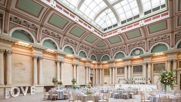 A grand hall with multiple round tables set for a formal event, featuring a high, ornate ceiling and a large glass skylight. - Harbour Hotel Bristol (Bristol)