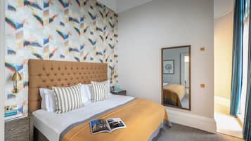 A neatly made bed with a striped pillow, a bedside table with a lamp, and a patterned wall.