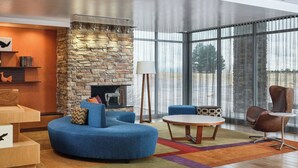 A modern living room with a stone fireplace, a blue sofa, a round coffee table, and a large window with curtains. - Fairfield Inn & Suites by Marriott Sidney (Sidney)