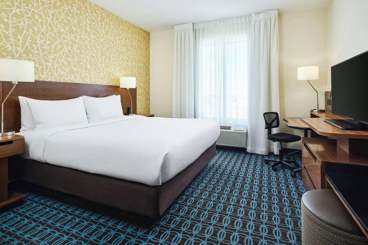 A hotel room with a large bed, a desk with a chair, a television, and a window with curtains.