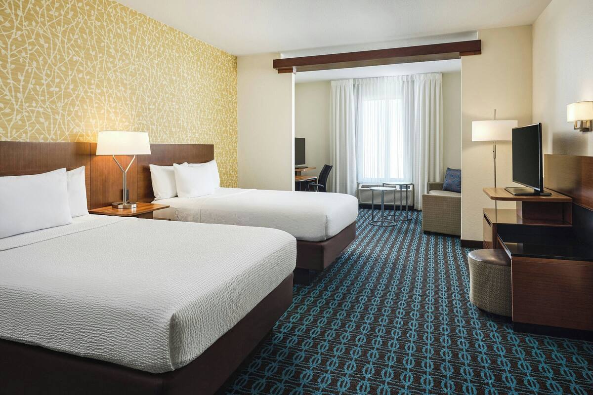 A hotel room with two beds, a desk, a chair, a TV, and a bathroom.