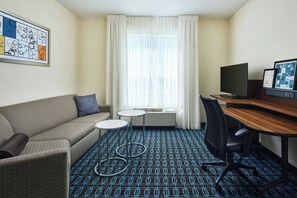 A hotel room with a sofa, two small tables, a desk with a computer, a chair, and a patterned carpet. - Fairfield Inn & Suites by Marriott Sidney (Sidney)