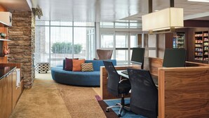A modern office space with a curved blue sofa, wooden desks, and a stone accent wall. - Fairfield Inn & Suites by Marriott Sidney (Sidney)