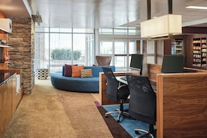 A modern office space with a curved blue sofa, wooden desks, and a stone accent wall. - Fairfield Inn & Suites by Marriott Sidney (Sidney)