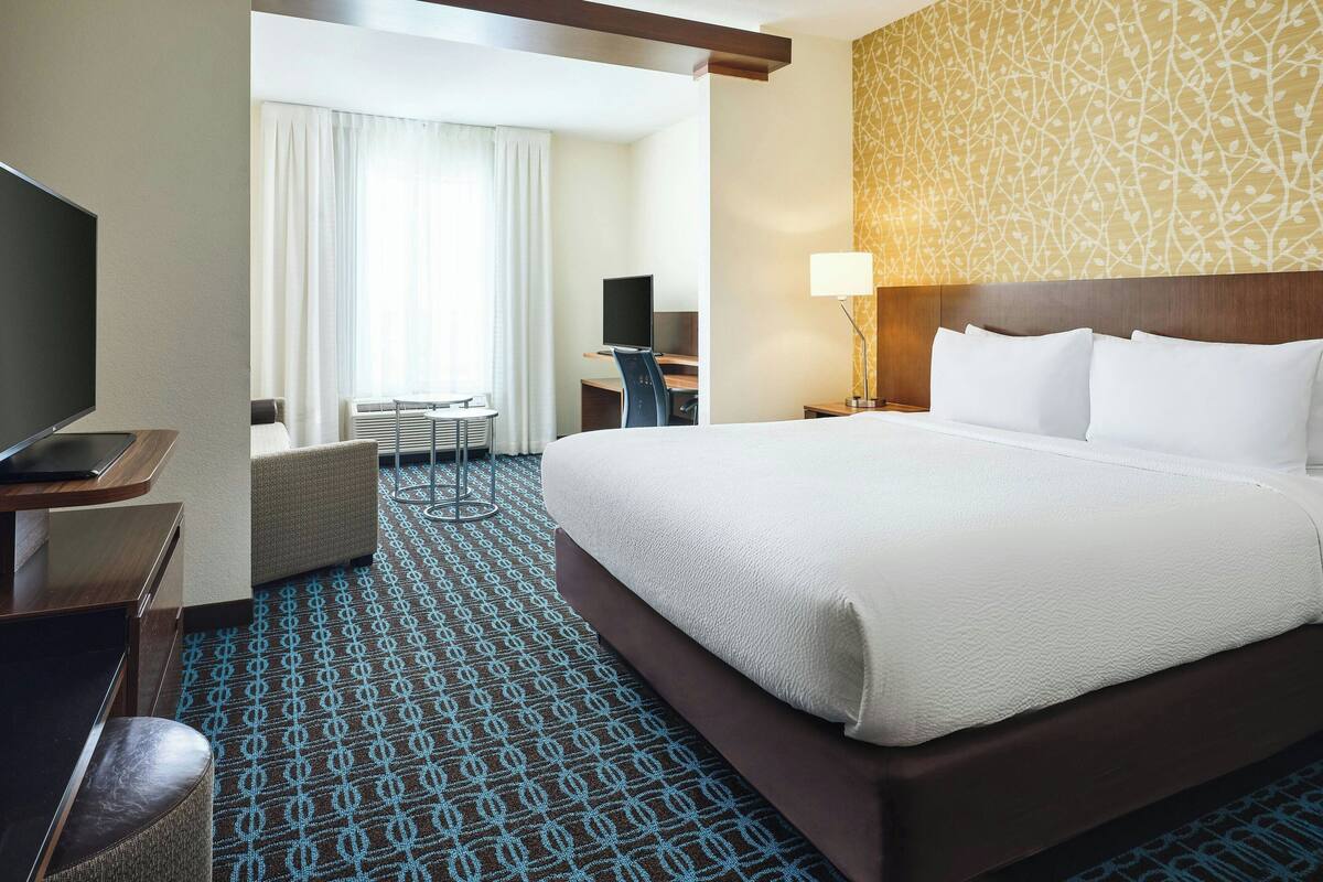 A hotel room with a large bed, a desk with a computer, a chair, and a TV.